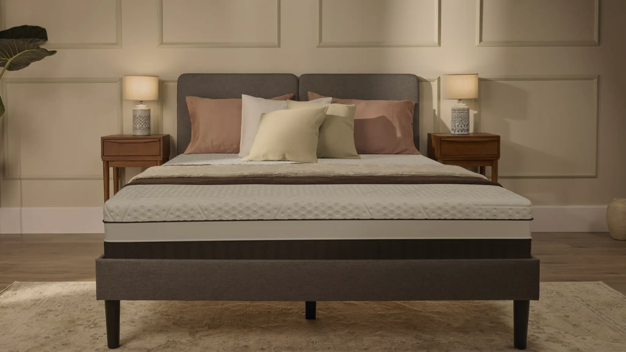 The Emma Luxe ViscoCool made up on a grey upholstered bed base, seen from the foot of the bed in a lamp-lit bedroom.