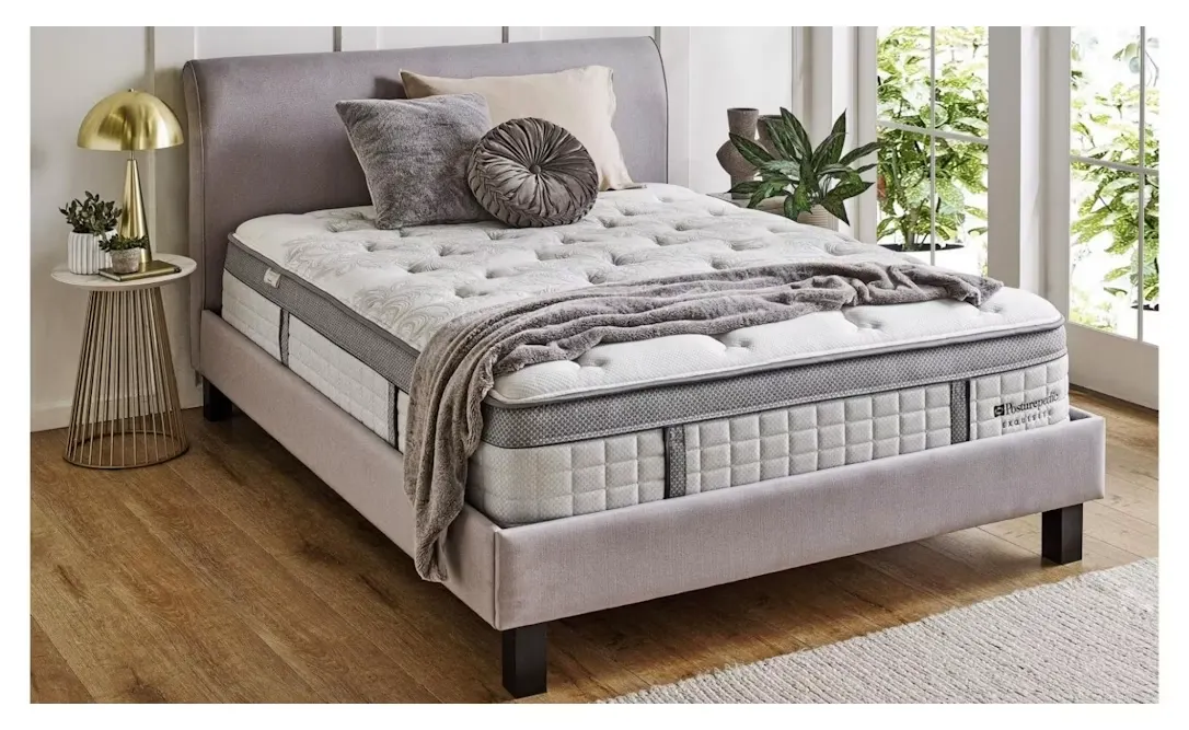 The Sealy Posturepedic Exquisite Rosewood made up with a grey throw, showing the tufted pillow-top and quilted side panels.
