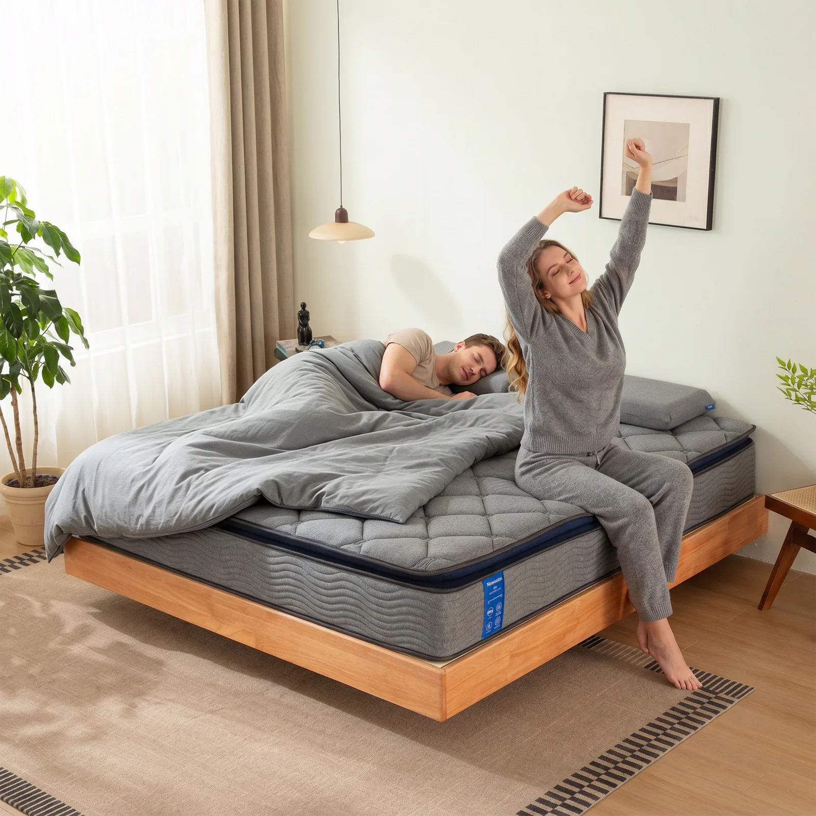 A woman stretching as she sits up on the Newentor Hybrid Mattress Pro while her partner sleeps on, on a timber bed frame in a bright bedroom.
