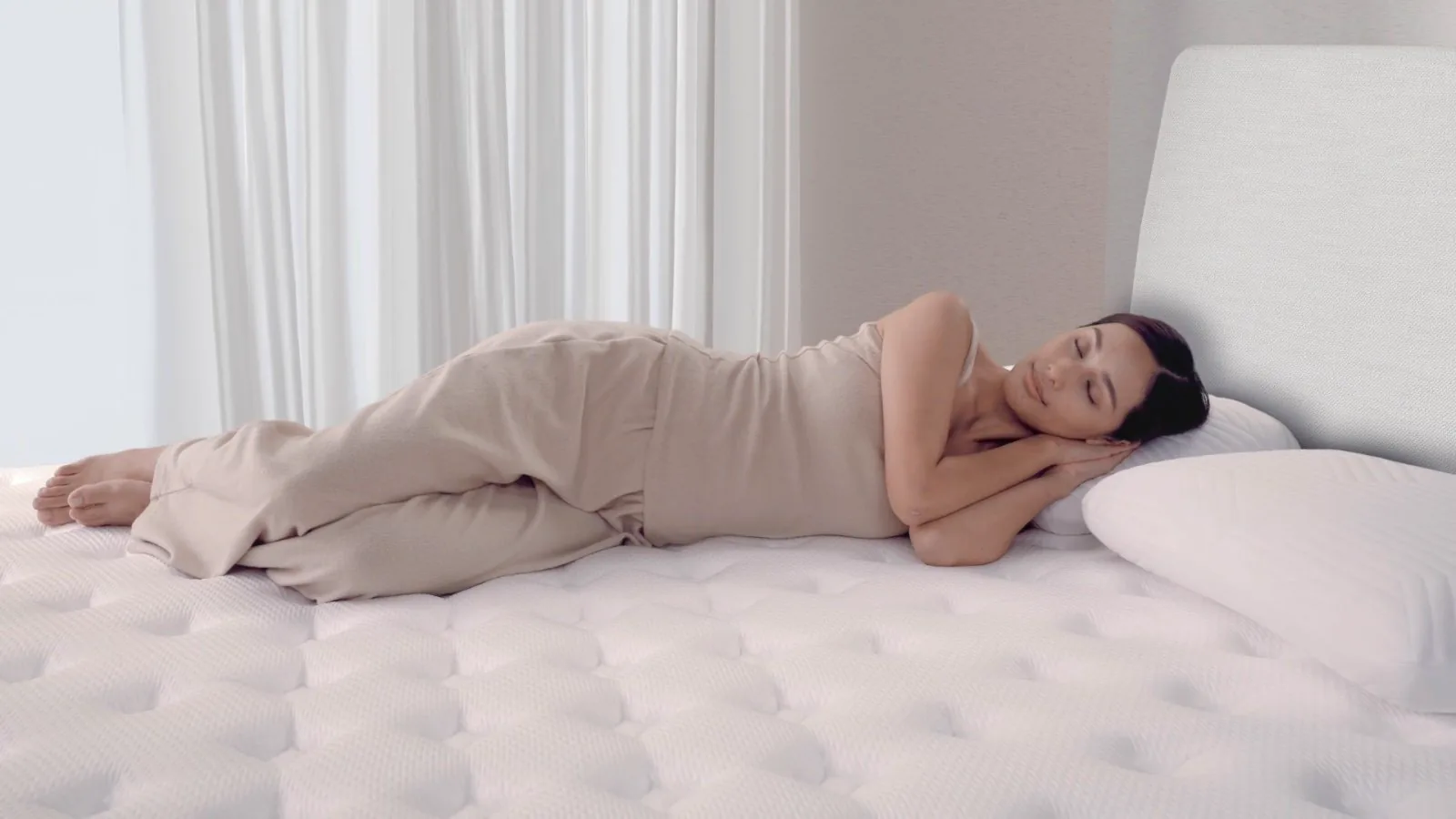 A woman asleep on her side on the Origin LumbarCloud, showing its white quilted pillow-top.
